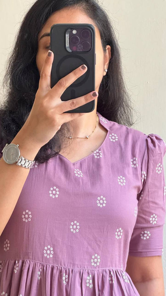 Person wearing a purple dress with white floral patterns, holding a phone with a black case.