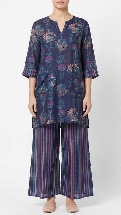 Woman wearing a navy blue floral patterned top and striped pants on a white background