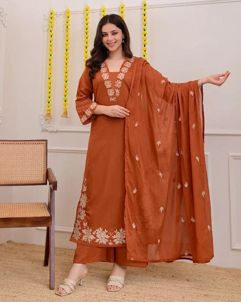 Woman wearing a rust-colored traditional outfit with white embroidery in a room.